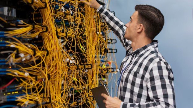 IT technician adjusting tangled network cables in a server rack while holding a tablet.
